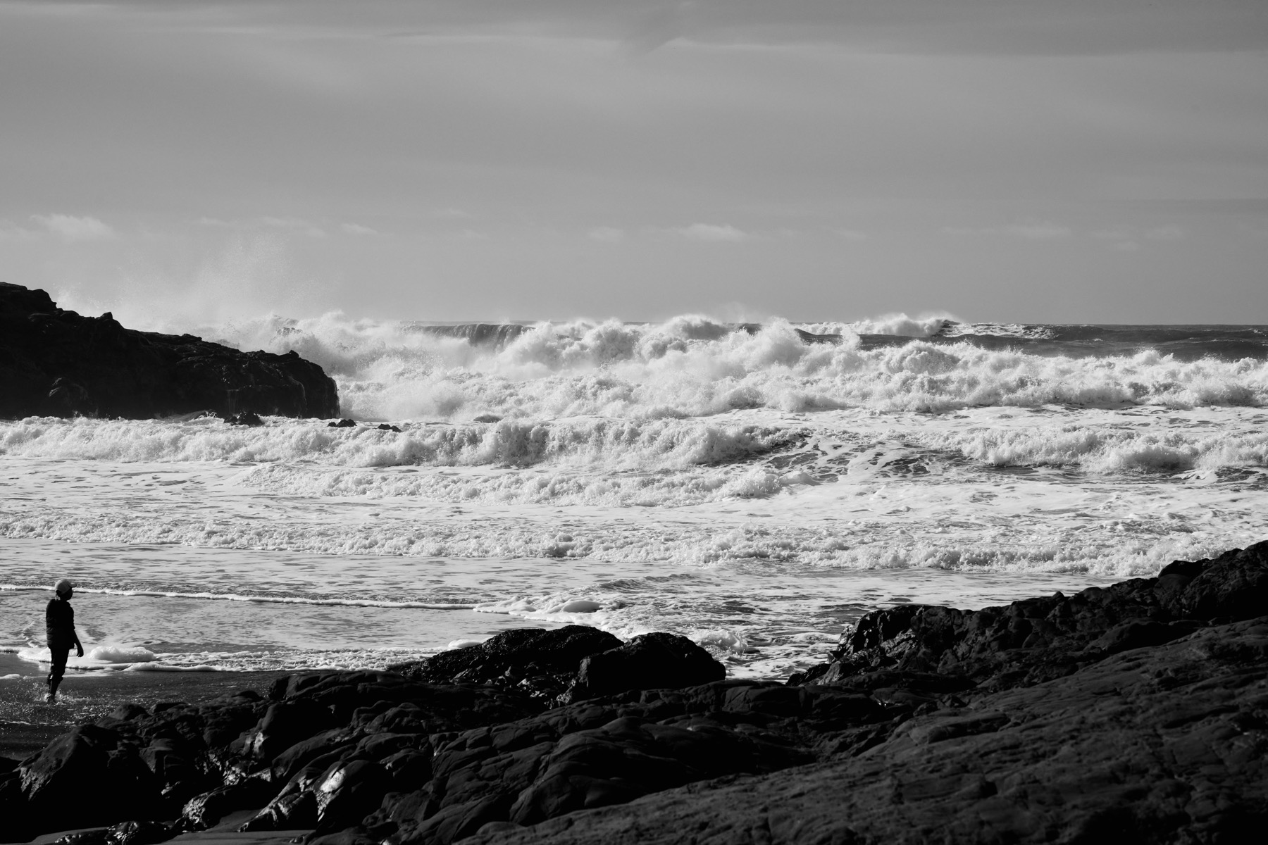 A person stands in the foreground looking at so many waves.
