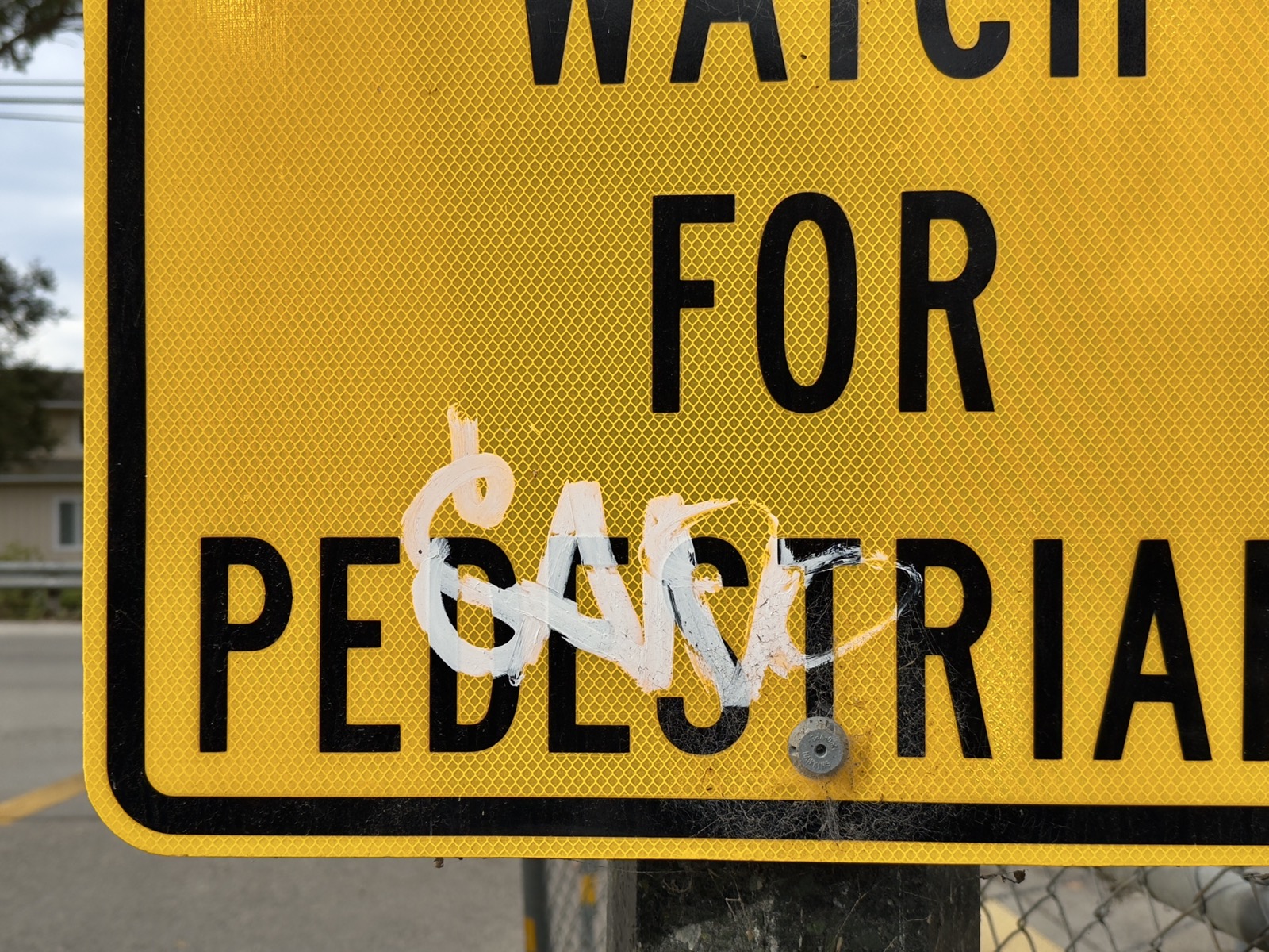 A fat white paint marker tagged EANO over a yellow pedestrian crosswalk sign.