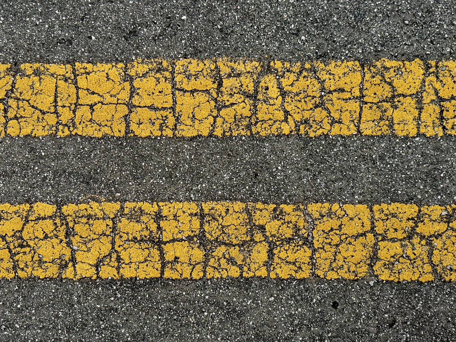 Two old, worn out, parallel yellow road lines, cracked and weakened but still serving.