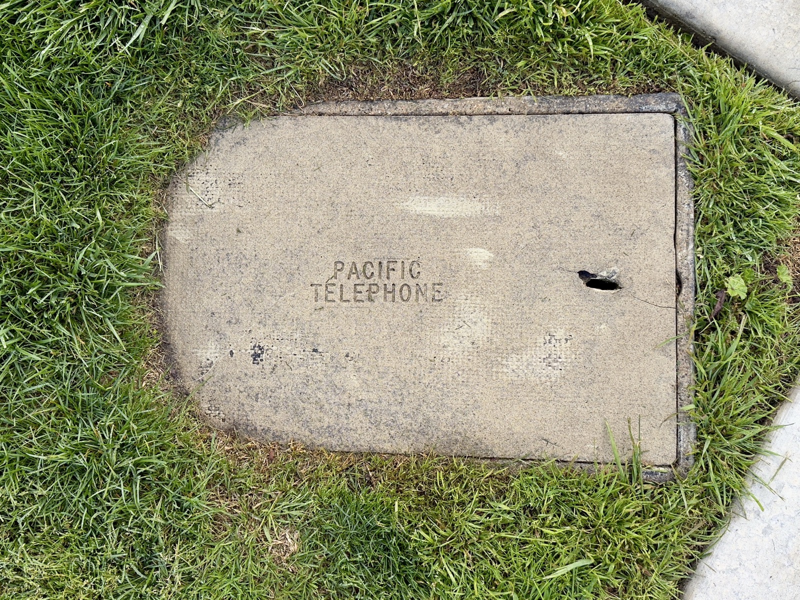 A cement utility cover in the lawn. On the face it says 'Pacific Telephone'